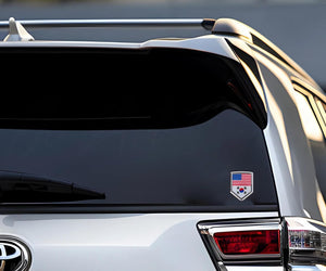 Xalvoria dual flag emblem sticker featuring the United States and South Korea flags applied on the rear window of a white SUV, shield-shaped chrome-style badge shown in an outdoor vehicle scene