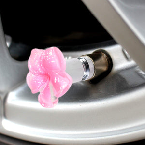 Close-up view of the pink plumeria valve stem cap installed on a car tire valve – Xalvoria