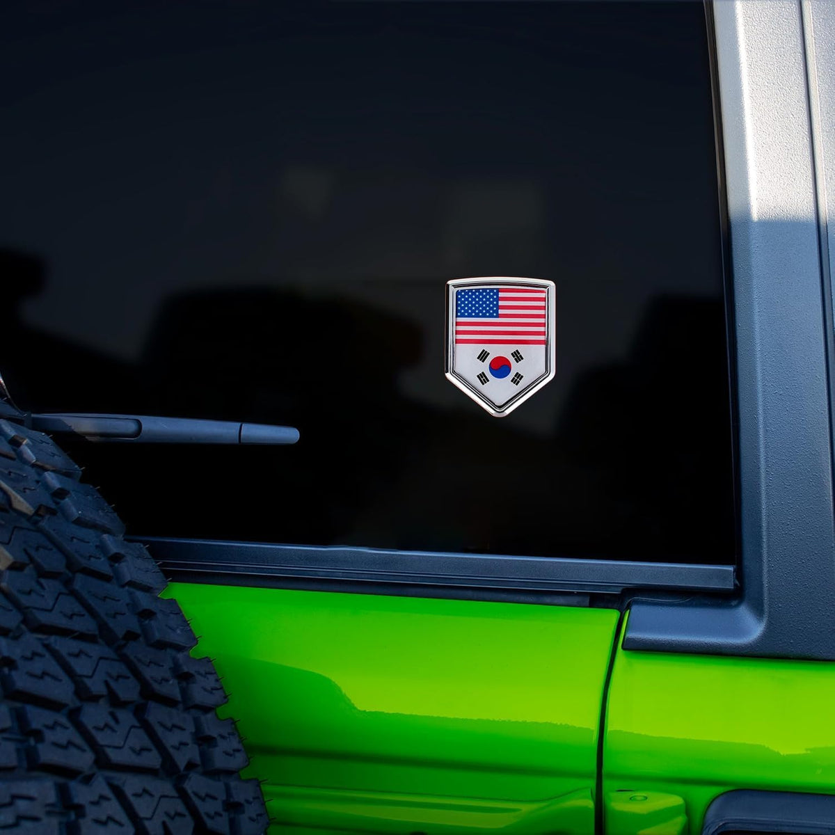 Xalvoria dual flag car emblem sticker with United States and South Korea flags displayed on a vehicle rear window, shield-shaped chrome-style automotive badge in real car scene
