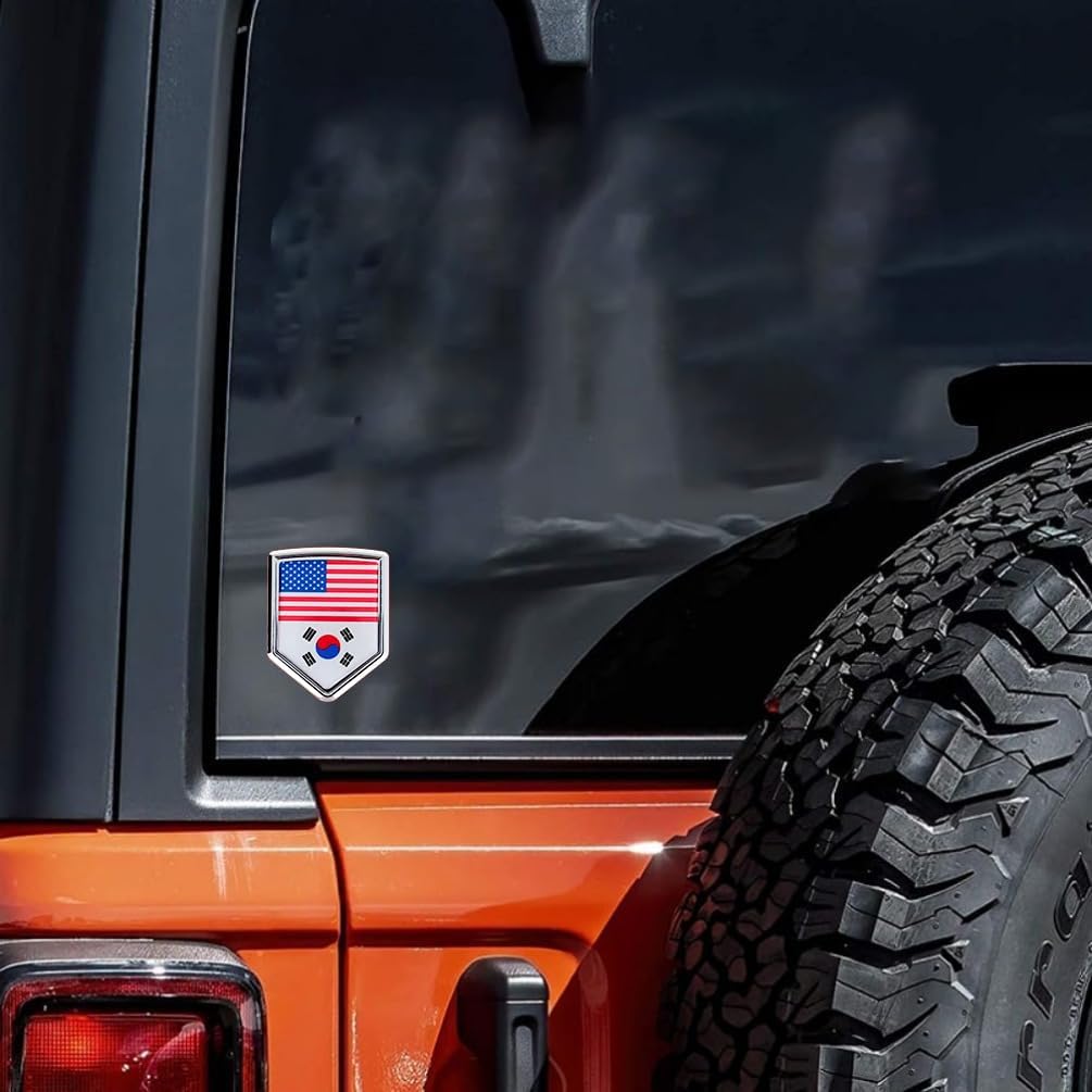 Xalvoria dual flag emblem sticker with United States and South Korea flags displayed on the rear side window of an orange Jeep, shield-shaped chrome-style badge applied on automotive glass in a real vehicle scene
