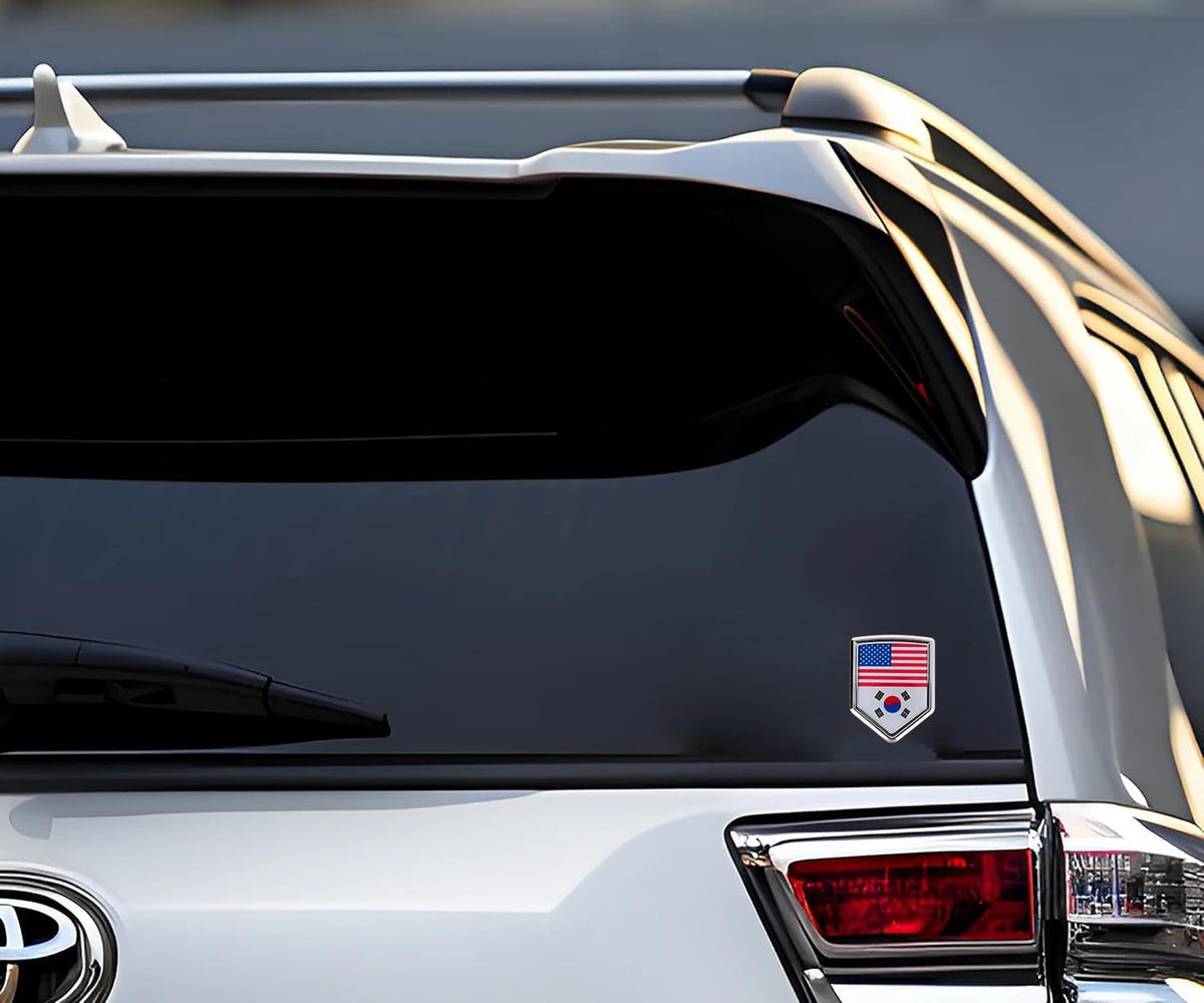 Xalvoria dual flag emblem sticker featuring the United States and South Korea flags applied on the rear window of a white SUV, shield-shaped chrome-style badge shown in an outdoor vehicle scene
