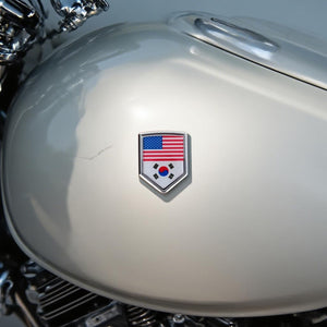 Xalvoria dual flag emblem sticker featuring United States and South Korea flags applied on a motorcycle fuel tank, shield-shaped chrome-style badge shown in real motorcycle scene
