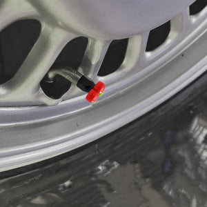 Close-up of a cherry-shaped valve stem cap installed on a car wheel, showing the red fruit design and secure fit on the tire valve.