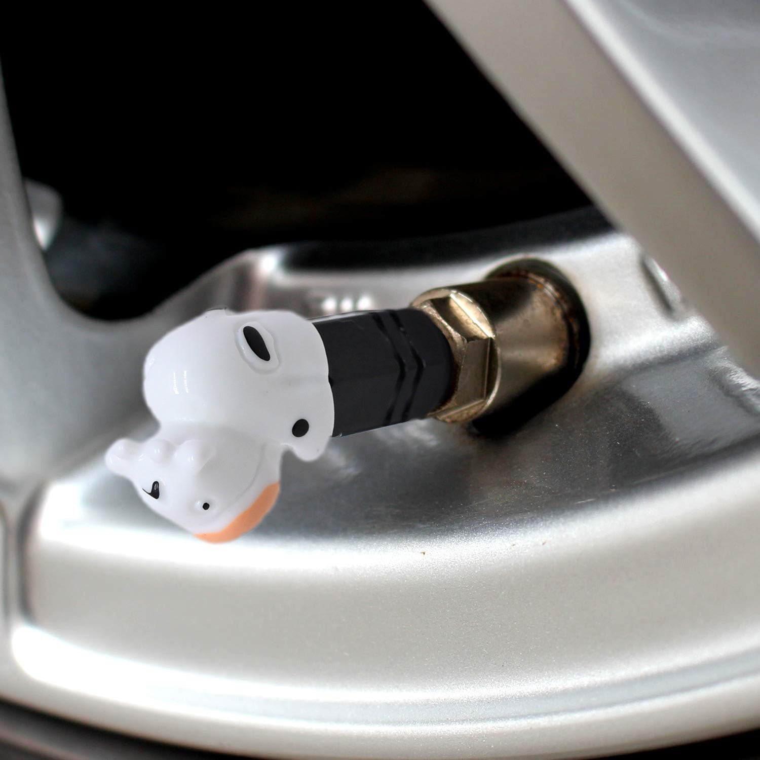 Close-up of a cow-shaped valve stem cap on a car rim, highlighting the white cow design and snug fit on the tire valve.