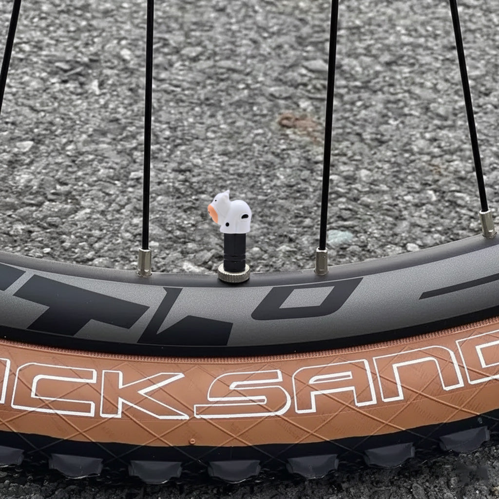 Cow-shaped valve stem cap installed on a bicycle wheel, showing the cute white cow design in real outdoor use.