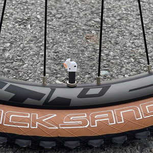 Cow-shaped valve stem cap installed on a bicycle wheel, showing the cute white cow design in real outdoor use.