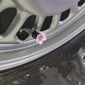 Xalvoria pink cherry blossom valve stem cap shown installed on a car wheel valve in a close-up scene.