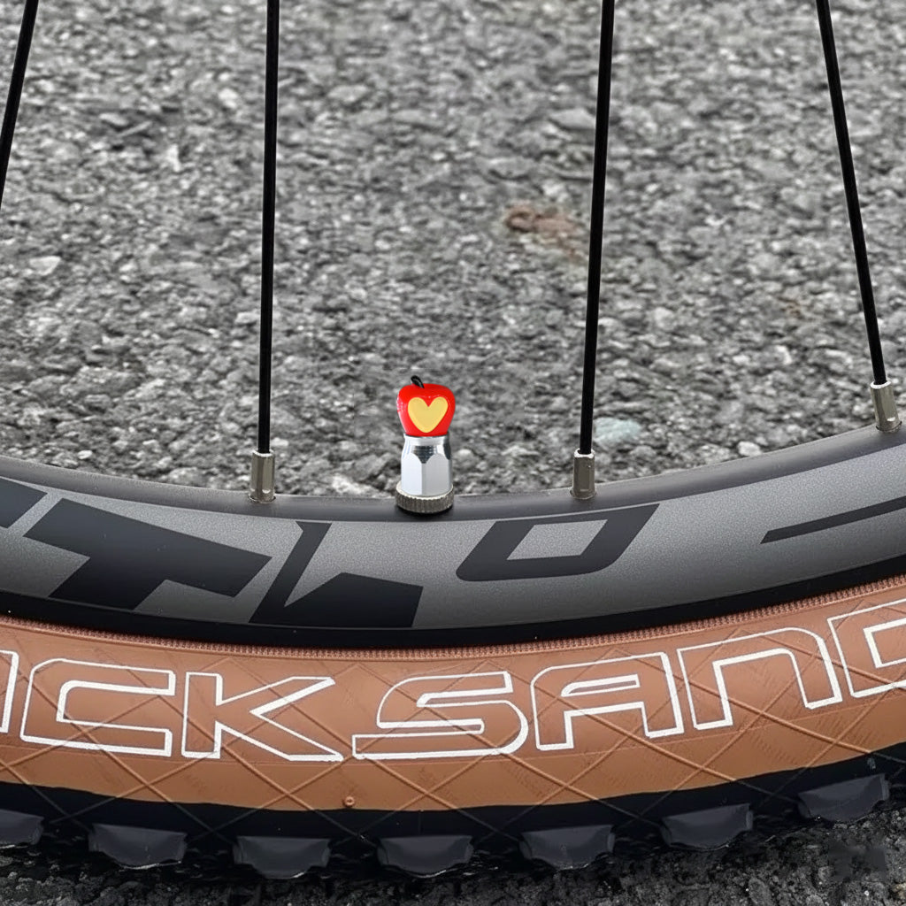 Xalvoria red Apple Core valve stem cap mounted on a bicycle wheel in an outdoor riding scene.